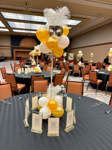 Elegant masquerade-themed centerpiece with gold and white balloons and feathers.