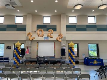 Indoor event setup with 2022 balloons and chairs arranged facing a stage.
