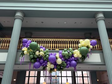 Colorful balloon garland in green, purple, and cream decorates a balcony.