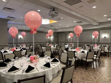 Elegant banquet hall decorated with pink balloons and black napkins for an event.