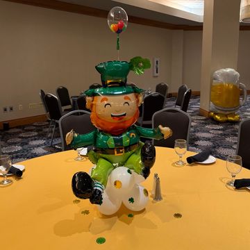 A festive leprechaun balloon centerpiece on a yellow-covered table.