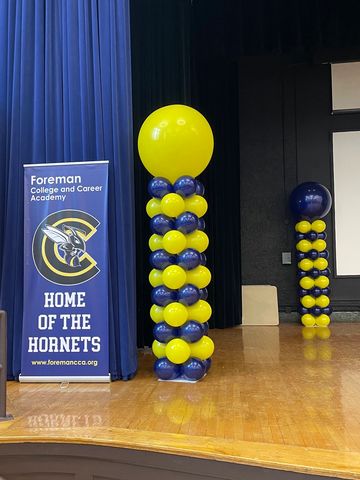 Yellow and blue balloon pillars on a stage with a school banner.