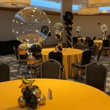 Elegant event room with black and gold balloon centerpieces on yellow tables.