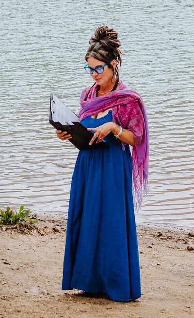 Woman standing by water reading from a clipboard.