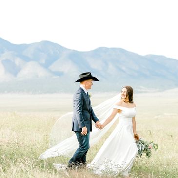 Bride and groom holding hands outdoors with mountains in background.