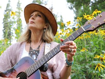 Woman playing guitar outdoors among yellow flowers.