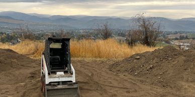 Mountains in the background with dirt moved all around a skid steer that has levelled the ground.