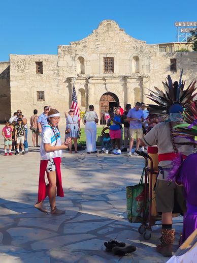 People gathered near the Alamo with dancers in traditional attire.
