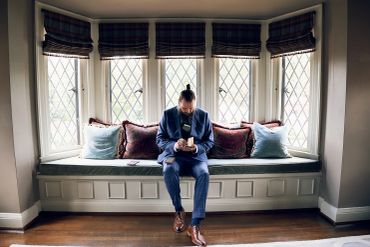 A man in a suit sitting on a window seat checking his phone.