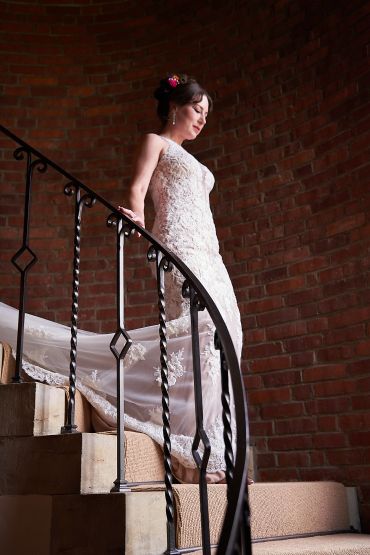 Bride in white lace gown descending staircase.