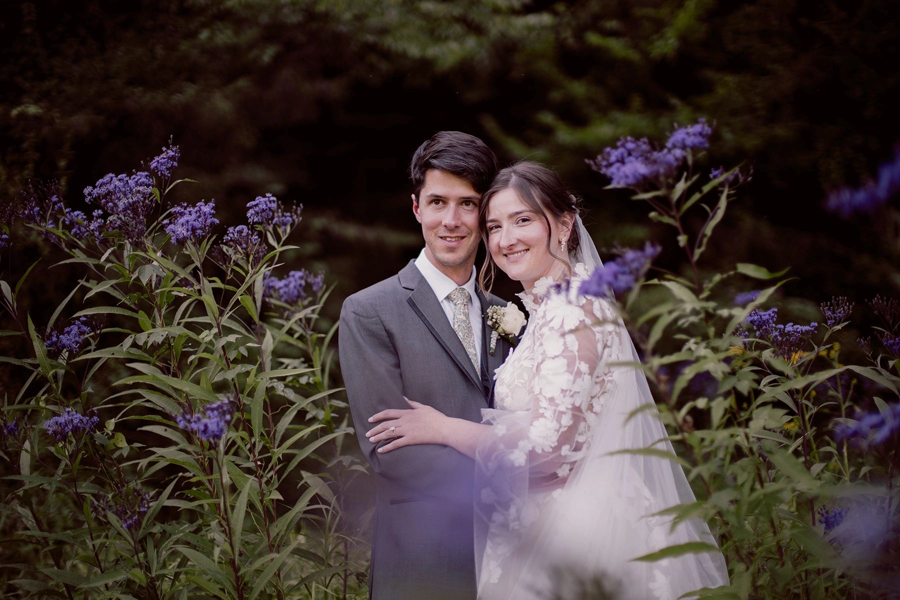 Newlywed couple embracing among purple flowers on their wedding day.