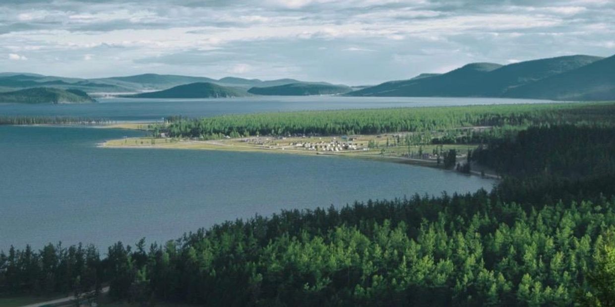 A serene lake surrounded by dense forests and distant mountains under a cloudy sky.