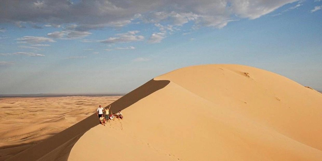 Group of people enjoying a sunny day on a large sand dune in the desert.