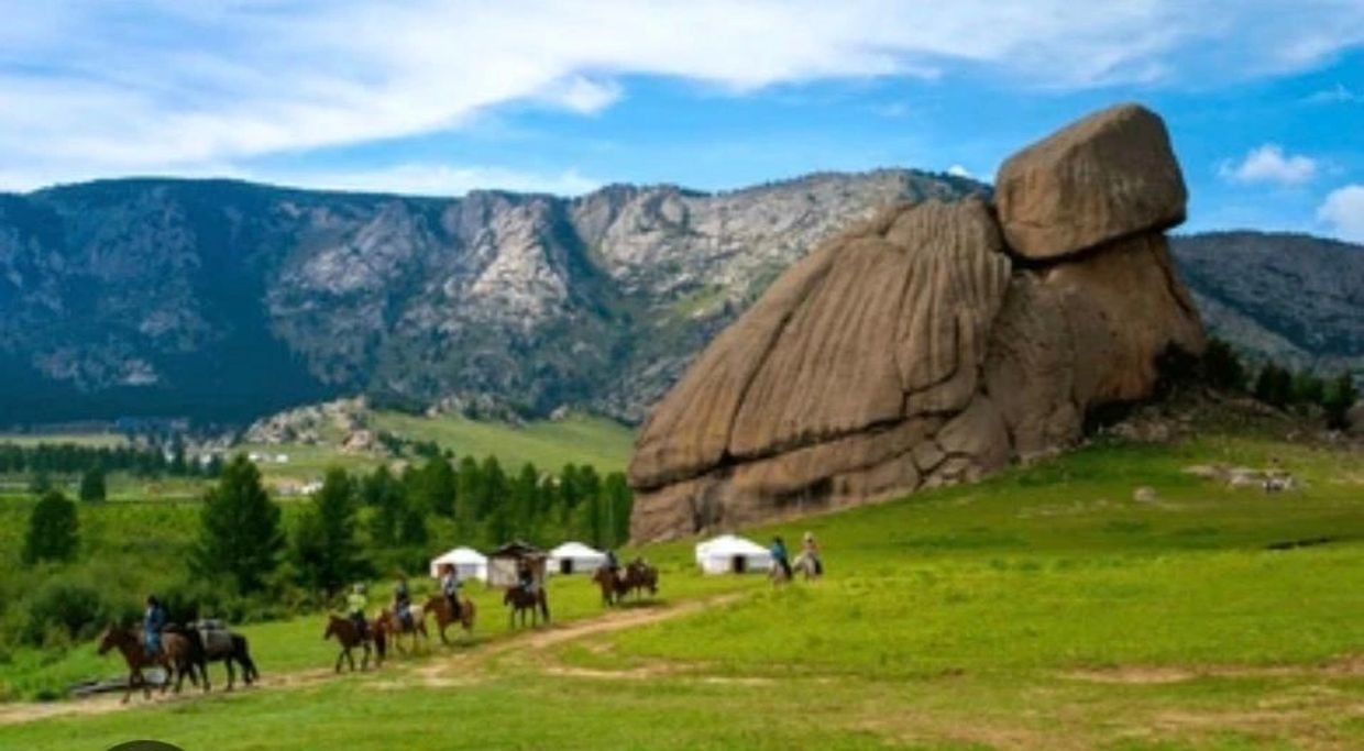 Group riding horses near large rock formation and yurts in a scenic mountainous area.