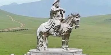 A statue of a rider on a horse in a vast green field with mountains in the background.