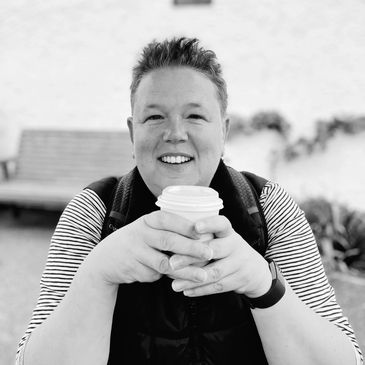 Smiling person holding a cup, sitting outdoors in black and white.