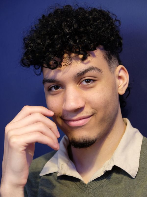 Young man with curly hair smiling against a blue background.