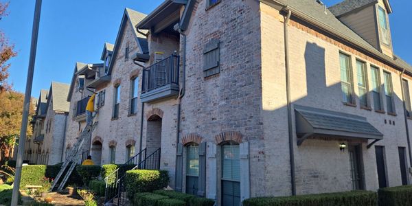 Workers on ladders maintaining a multi-unit brick townhouse with manicured bushes.