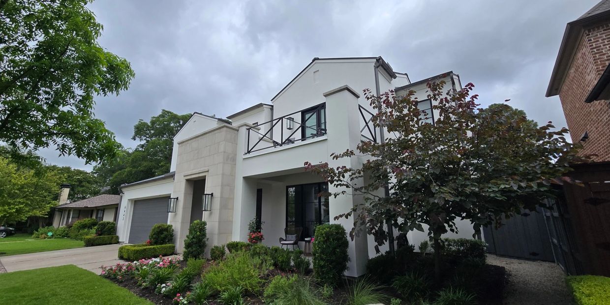 Modern two-story white house with lush garden and overcast sky.