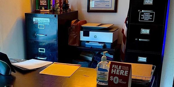 An office desk with files, hand sanitizer, and tax service sign.