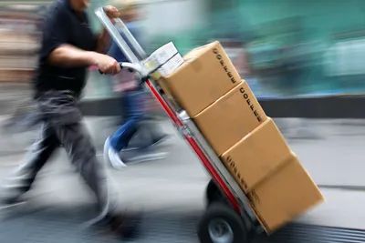 Person moving cardboard boxes with a hand truck.