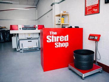 A bright red sign for The Shred Shop in a clean room with shredding equipment.
