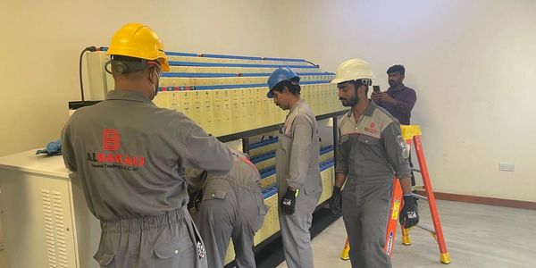 Workers in safety gear inspecting electrical equipment indoors.