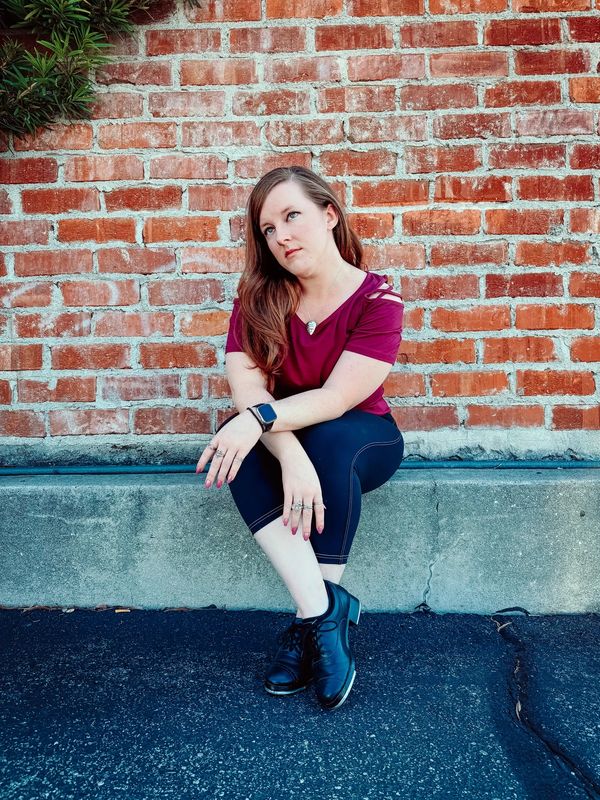 Woman sitting against a brick wall, looking pensive.