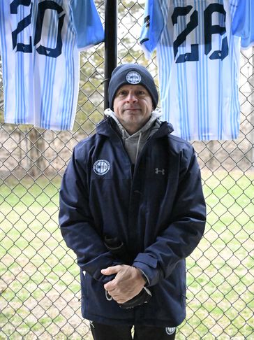 Man standing in front of a fence with hanging sports jerseys.