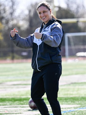 A woman in sportswear gestures enthusiastically on a soccer field.