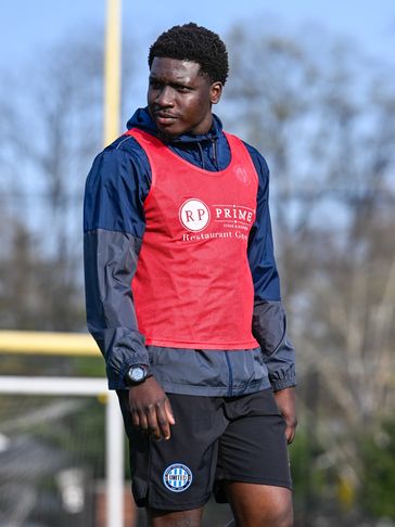 Athlete in training gear with a red vest on a sports field.