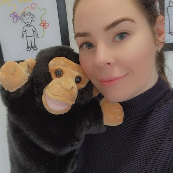 A woman smiling with a plush monkey puppet on her hand.