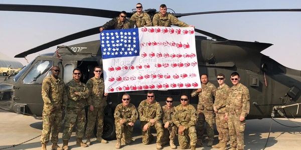 Group of soldiers posing with a handprint American flag in front of a helicopter.