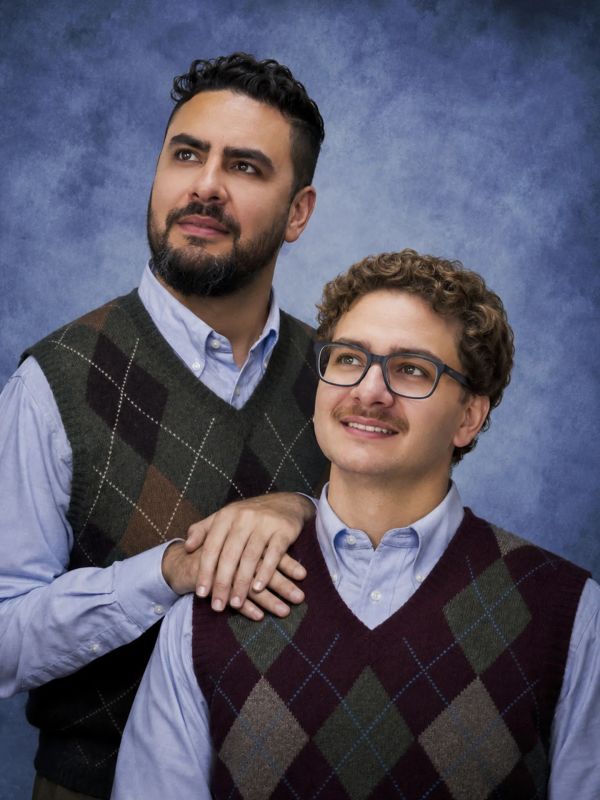 Two men in argyle sweater vests posing against a blue backdrop.