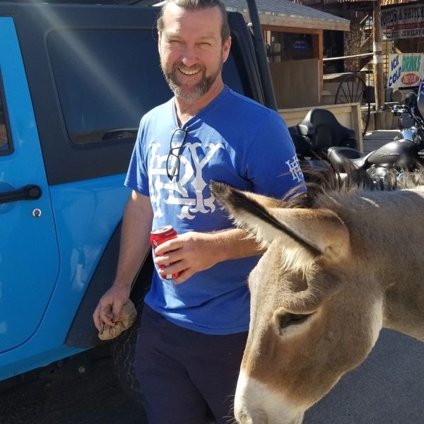 Man smiling near a donkey and blue vehicle.