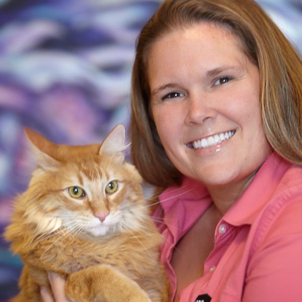 Woman smiling and holding a fluffy orange cat.