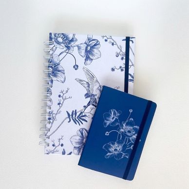Two floral-patterned notebooks, one white and one blue, on a white background.