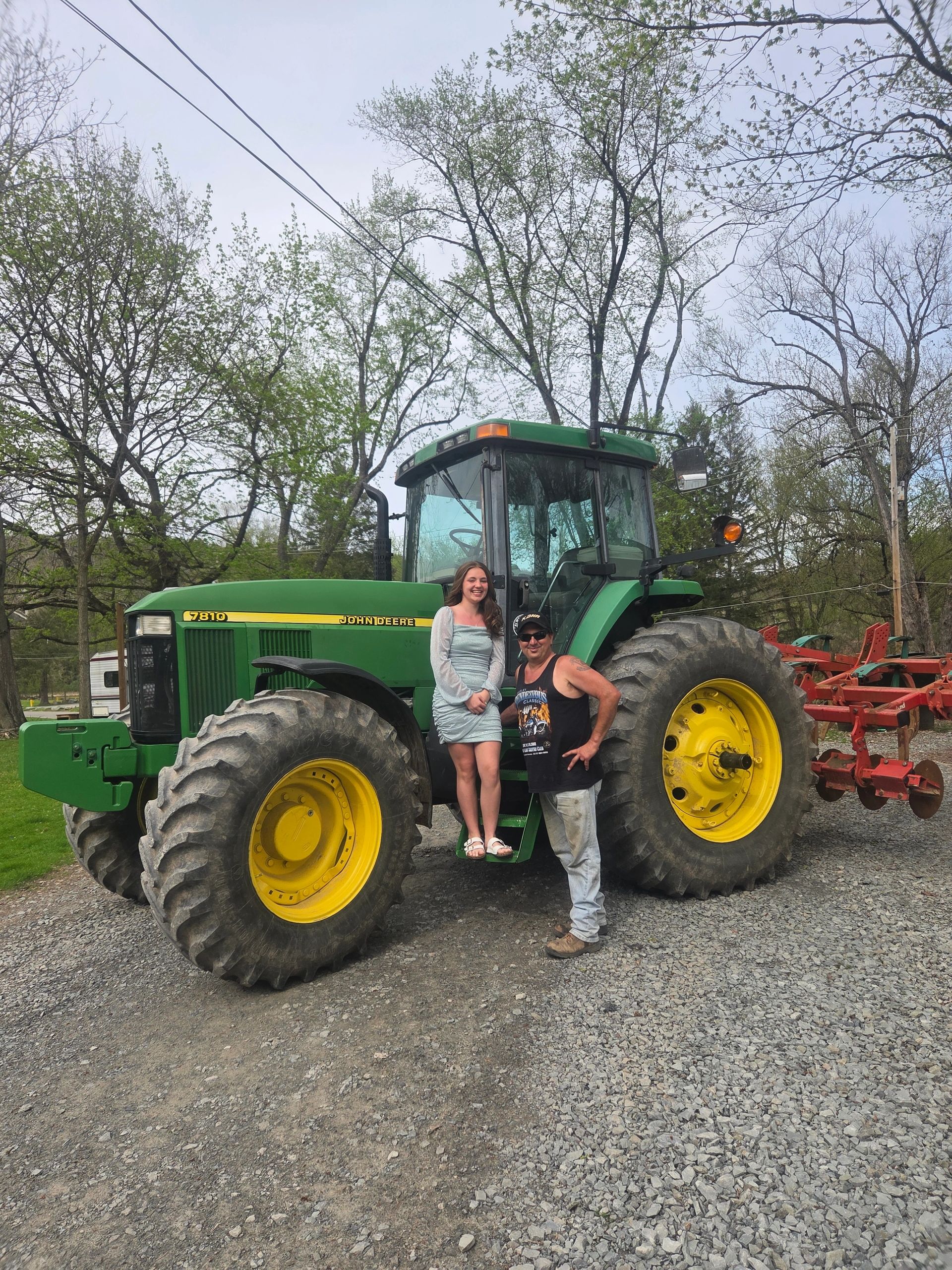 A young woman and a man posing by a green John Deere tractor.