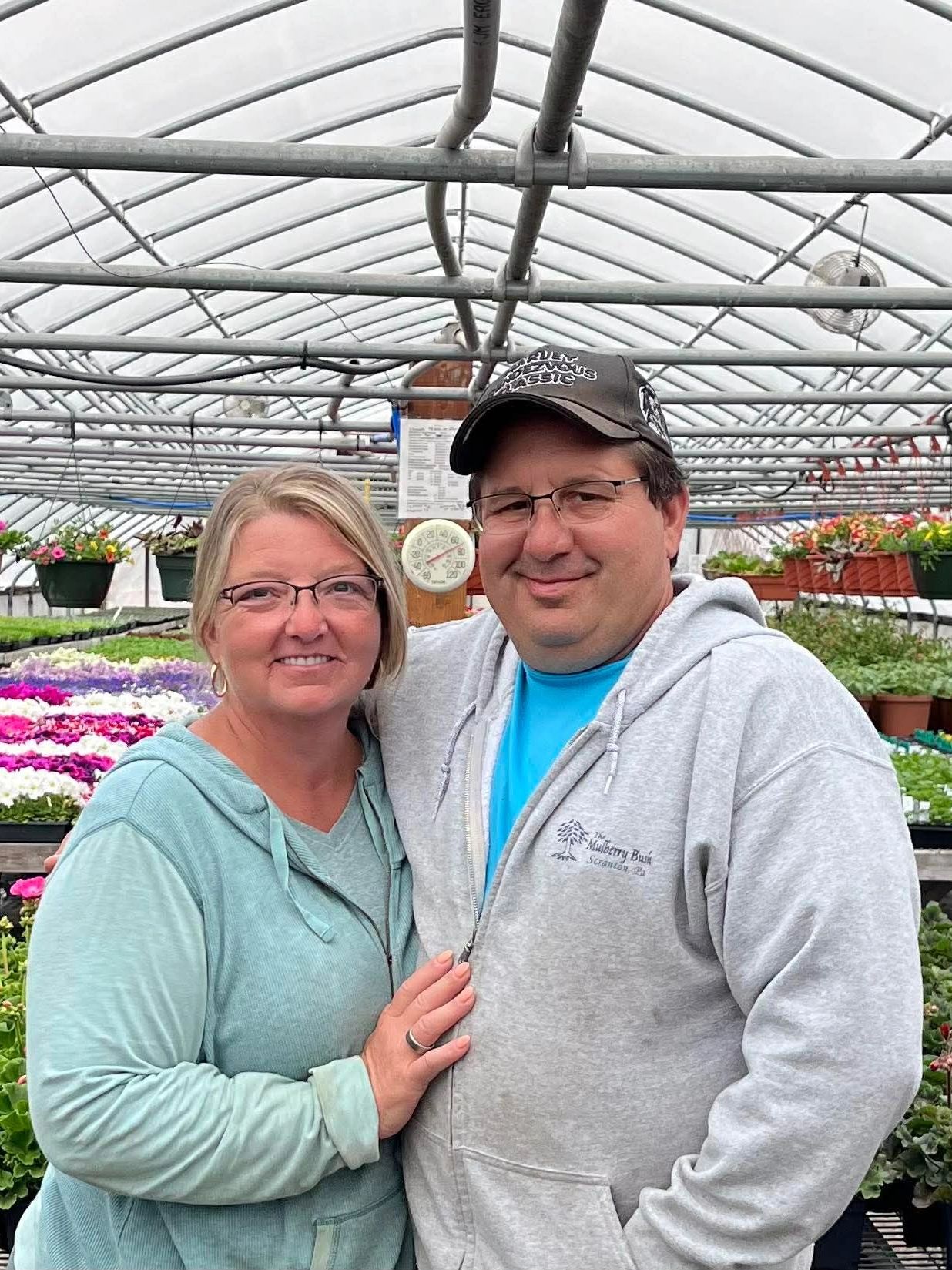 A couple smiling inside a greenhouse filled with colorful flowers.