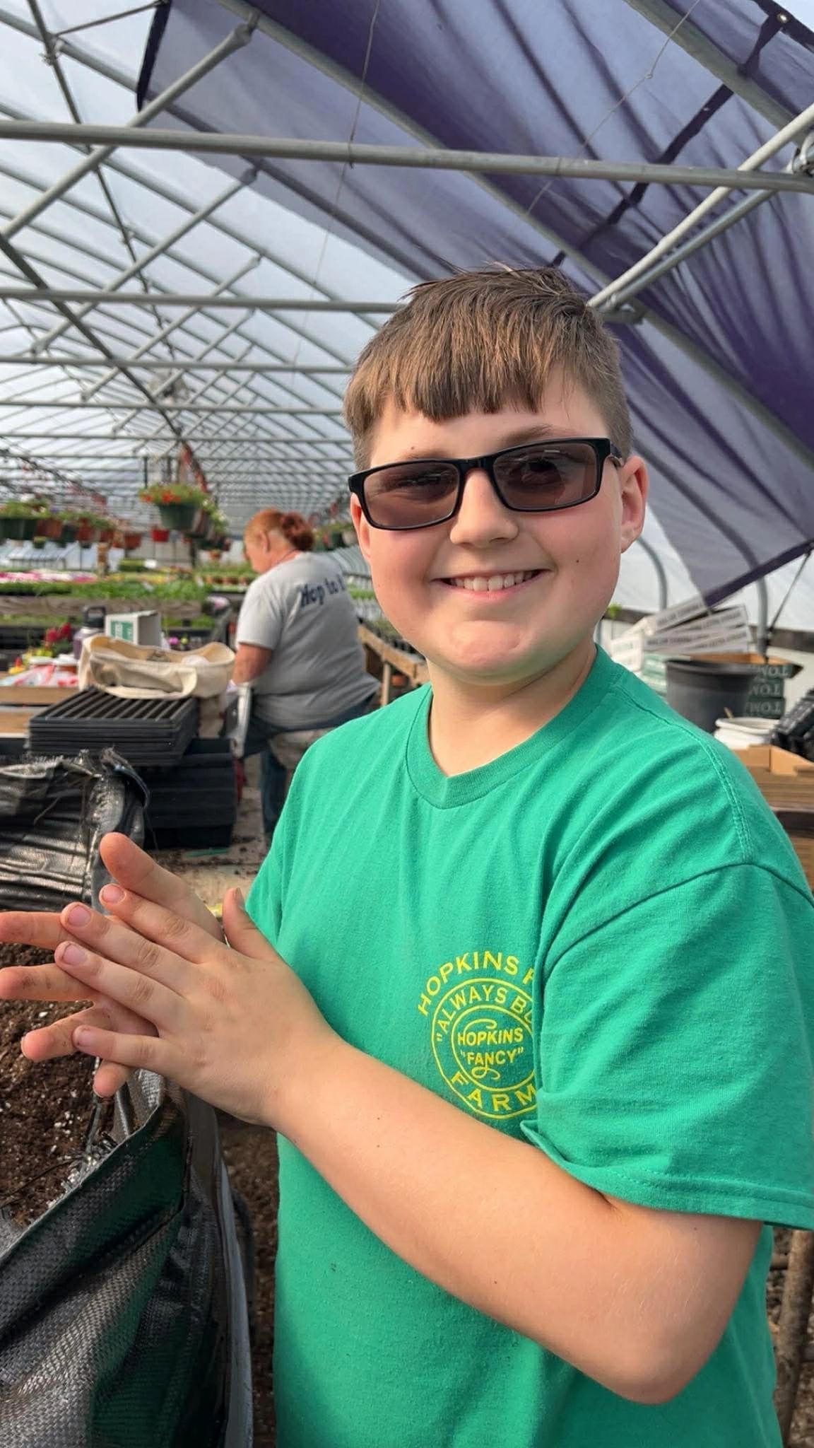 Smiling boy in sunglasses planting seeds at a greenhouse farm.