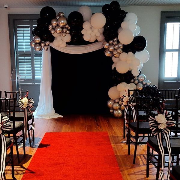 Elegant event setup with black and white balloons, black chairs, and a red carpet.