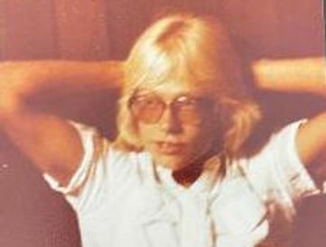 Man with short blonde hair and glasses leaning on wall