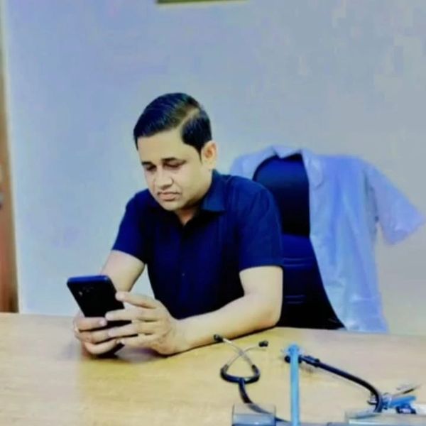 Man sitting at desk looking at phone with stethoscope nearby.