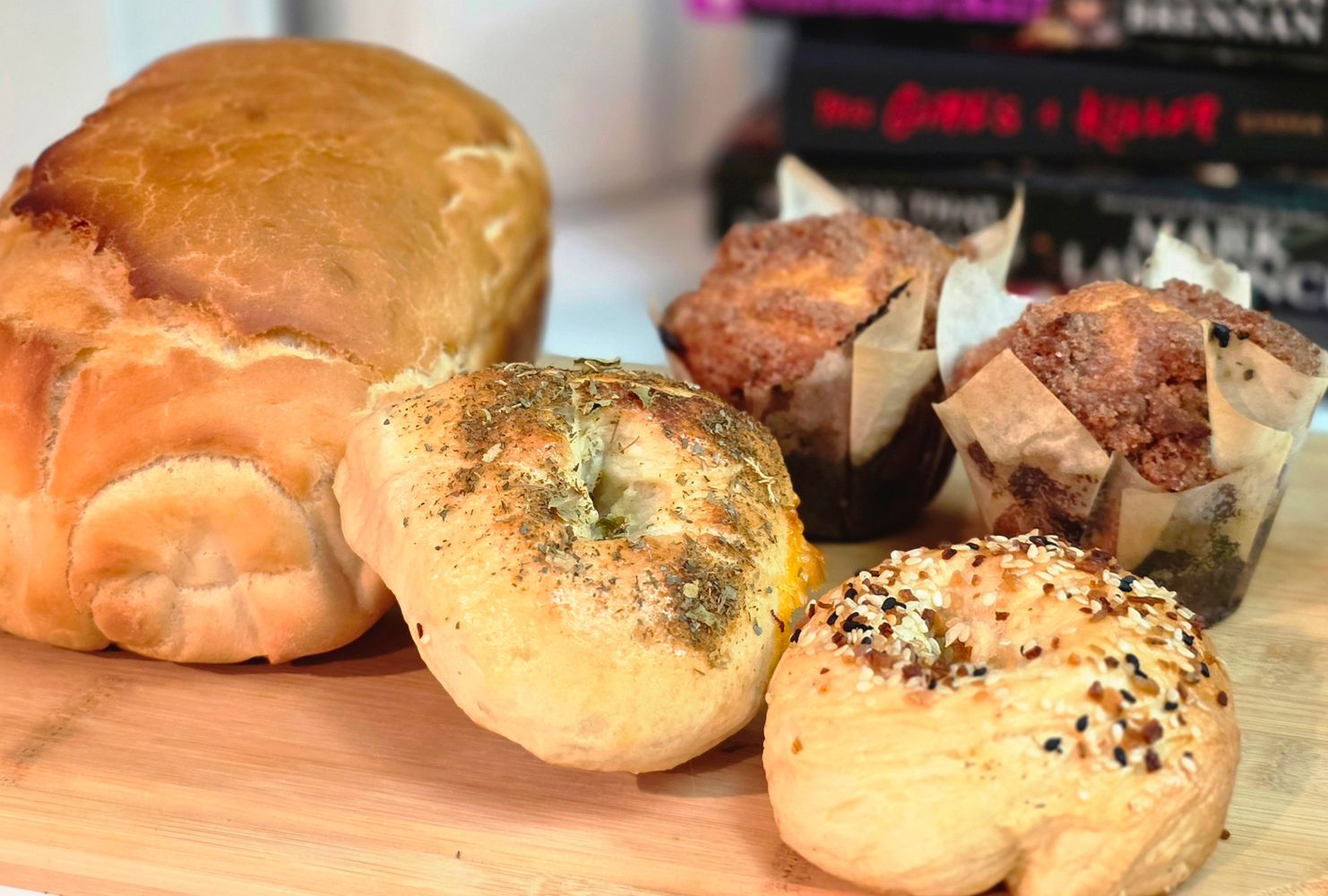 Freshly baked bread, bagels, and muffins on a wooden board.