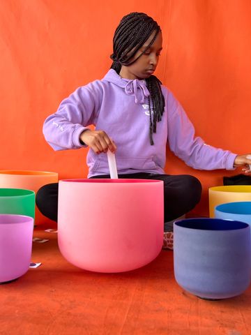 Woman playing colorful crystal singing bowls against an orange backdrop.