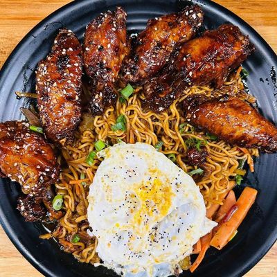 Grilled wings with noodles and a sunny-side-up egg.