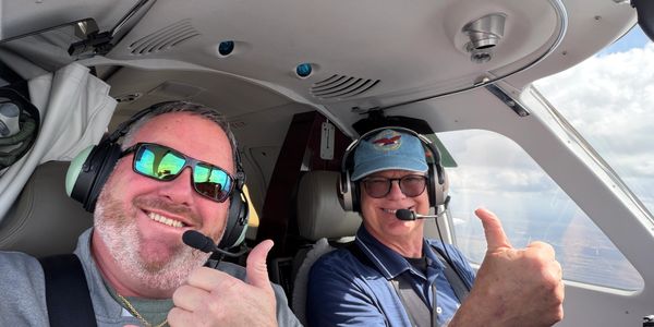 Two men in a cockpit giving thumbs up and smiling.