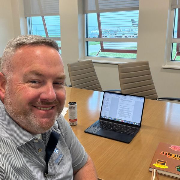 Man smiling in a conference room with a laptop and notebook on the table.