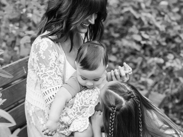 Mother holding baby with daughter looking on joyfully.