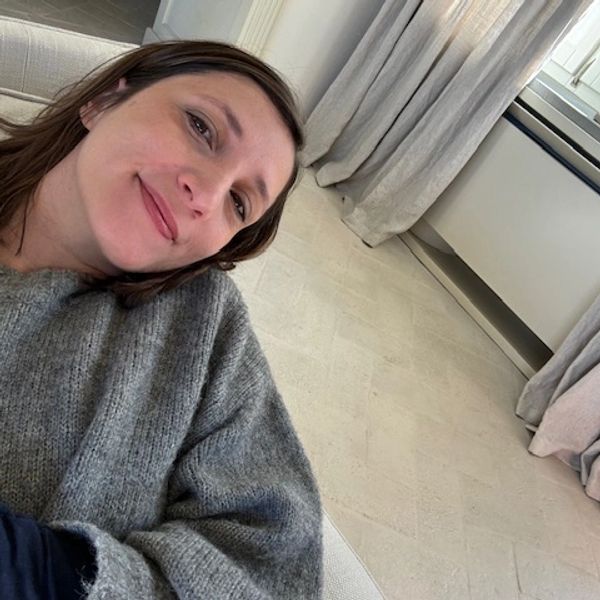 A woman in a cozy gray sweater relaxing on a couch near a window with curtains.
